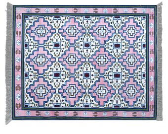 Puede incluir: Una alfombra de color rosa y azul con un diseño geométrico. La alfombra tiene un fondo blanco con un borde de color verde, rosa y azul. La alfombra tiene flecos en los cuatro lados.
