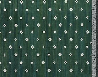 May include: A close-up of a green rug with a diamond pattern. The rug has a dark green background with lighter green vertical stripes. White diamond shapes are evenly spaced across the surface. The edge of the rug has a grey fringe.
