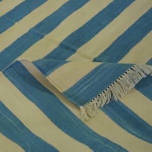 Puede incluir: Una alfombra de rayas azules y crema con un borde de flecos. La alfombra está hecha de un material suave y tejido.