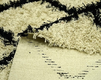 May include: A white and black rug with a geometric pattern. The rug has a fluffy texture and is made of natural fibers.