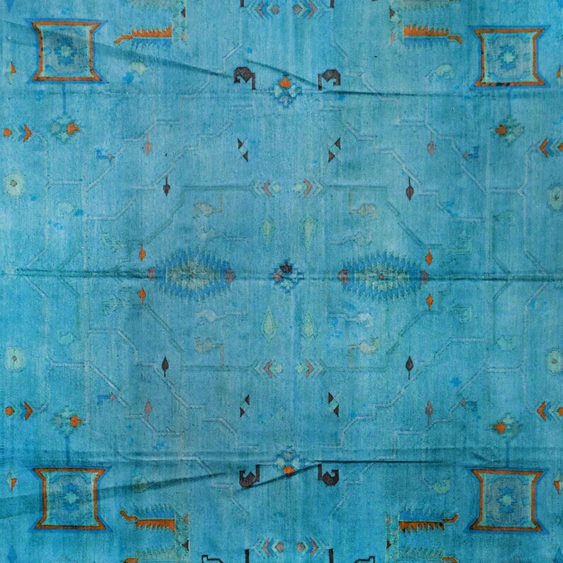 Op de afbeelding: Een vintage blauw tapijt met een geometrisch patroon in tinten oranje, blauw en zwart. Het tapijt heeft een versleten en vervaagde uitstraling, waardoor het een rustieke en antieke uitstraling heeft.
