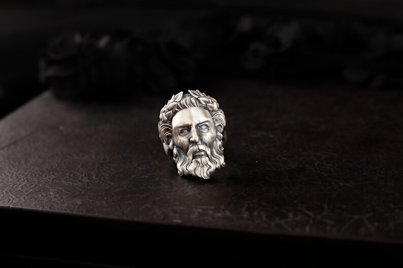 May include: A silver ring with a detailed design of a man's face with a beard and a laurel wreath on his head.