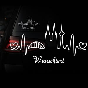 Könnte beinhalten: Weißer Vinyl-Autoaufkleber mit einem stilisierten Herzschlag-Design mit der Silhouette des Kölner Doms und einer Brücke. Der Text "Köln am Rhein" und "Wunschtext" sind ebenfalls enthalten. Der Aufkleber ist auf einem schwarzen Auto angebracht.