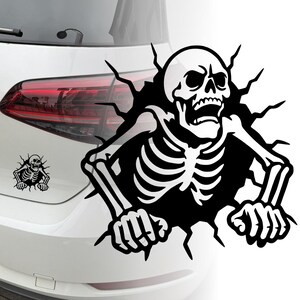 Op de afbeelding: Zwart-witte skelet auto sticker. Het skelet lijkt door het oppervlak te breken. Een kleinere versie van hetzelfde ontwerp staat links. De sticker is aangebracht op een witte auto.