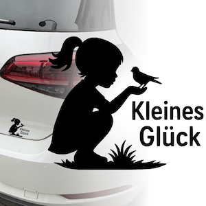 Può includere: Adesivo con silhouette nera di un bambino accovacciato che tiene in mano un uccello. Il testo "Kleines Glück" è visualizzato in bianco. Una versione più piccola dell'immagine è a sinistra.