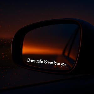 Könnte beinhalten: Ein Autospiegel mit dem weißen Text "Drive safe ♡ we love you". Der Spiegel spiegelt einen orangefarbenen und dunkelblauen Sonnenuntergang wider. Der Spiegel ist schwarz.