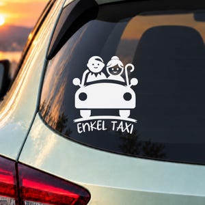 Könnte beinhalten: Ein weißer Autoaufkleber mit einer stilisierten Grafik von zwei Personen in einem Auto, wobei eine Person einen Gehstock hält. Unter der Fahrzeuggrafik ist der Text ENKEL TAXI in einer fetten, serifenlosen Schrift auf der Heckscheibe gedruckt.