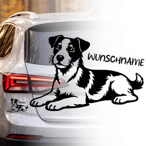 Può includere: Un adesivo per auto con un cane bianco e nero, raffigurante un Jack Russell Terrier, è esposto sul lunotto posteriore di un'auto. L'adesivo include il testo "WUNSCHNAME" e un adesivo più piccolo con il nome "BOBBY".