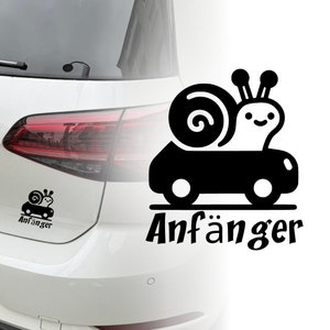 Könnte beinhalten: Schwarz-weißer Aufkleber eines Schnecken, der ein Auto trägt, mit dem Wort "Anfänger" darunter. Der Aufkleber befindet sich auf der Rückseite eines weißen Autos.