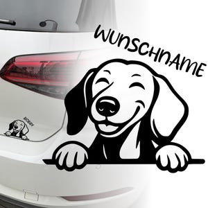 Könnte beinhalten: Schwarz-weißer Vinyl-Aufkleber eines lächelnden Hundes mit dem Text "WUNSCHNAME" darüber. Ein kleinerer Aufkleber des Hundes mit dem Namen "BOBBY" ist ebenfalls sichtbar. Die Aufkleber sind auf einem weißen Auto angebracht.