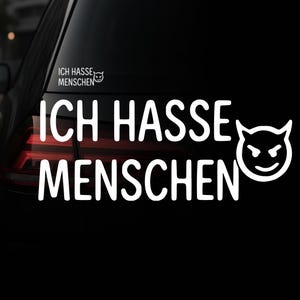 Puede incluir: Calcomanía de vinilo blanco con la frase alemana "ICH HASSE MENSCHEN" (Odio a la gente) en letras negritas, acompañada de un gráfico de cara de diablo. La calcomanía está aplicada a una ventana de coche negra.