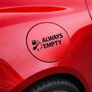 Könnte beinhalten: Ein schwarz-weißer Aufkleber mit den Worten "ALWAYS EMPTY" in einem kreisförmigen Design. Der Aufkleber befindet sich auf einem roten Auto und zeigt ein Kraftstoffanzeige-Symbol.