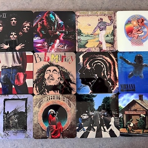 Puede incluir: Un conjunto de posavasos cuadrados con portadas de álbumes de varios artistas musicales. Los posavasos muestran imágenes de Queen, Bob Marley, Nirvana y otros. Los posavasos son cuadrados y tienen un acabado brillante.