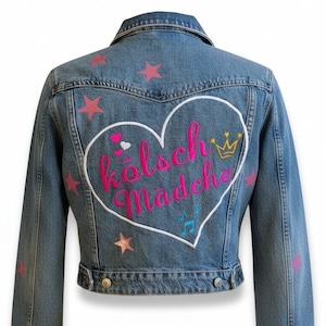 Könnte beinhalten: Eine blaue Jeansjacke mit einem großen, weiß gestickten Herz auf der Rückseite. Im Herz steht der rosa Schriftzug "Kölsche Mädche" zusammen mit einer kleinen gelben Krone, einem weißen Herz und blauen Noten. Rosa Sterne sind auf dem Rücken verteilt.