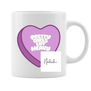Puede incluir: Taza de cerámica blanca con un gráfico en forma de corazón morado que dice "Pretty Girls Lift Heavy" en texto blanco. La taza también presenta el logotipo de Naduah's en negro. La taza tiene un asa curva.
