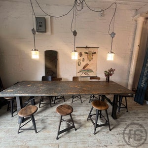 Könnte beinhalten: Ein großer Holztisch mit einem schwarzen Metallrahmen und sechs Hockern im Industriestil. Der Tisch steht in einem Raum mit weißen Wänden und einem Vintage-Insektenbild an der Wand.