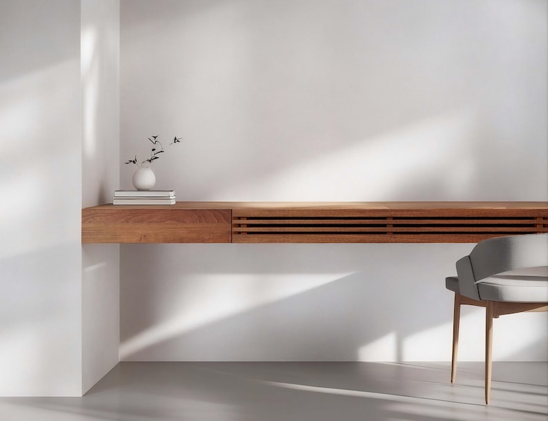 Peut inclure: Un bureau moderne en bois avec un tiroir int&eacute;gr&eacute; et un design &agrave; lattes. Un petit vase blanc avec des tiges noires et une pile de livres sont pos&eacute;s sur le bureau. Une chaise grise avec des pieds en bois est &agrave; proximit&eacute;. Le bureau est contre un mur blanc.
