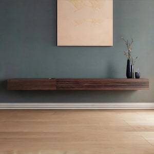 May include: A dark wood floating media console with a slatted front and a solid door. A dark blue vase with branches and a glass are on the console. A painting hangs above the console on a teal wall.