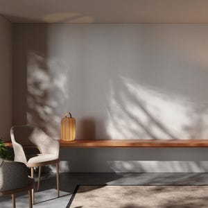 May include: Two beige chairs with wooden legs and a wooden shelf with a small wooden lamp on it. The wall is white with shadows from a window. There is a rug on the floor.