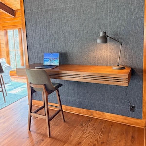 Peut inclure: Un bureau moderne en bois, fix&eacute; au mur, avec un ordinateur portable et une lampe de bureau. Le bureau a un design &agrave; lattes et est associ&eacute; &agrave; un tabouret de bar rembourr&eacute; vert. Le fond pr&eacute;sente un mur gris textur&eacute;.