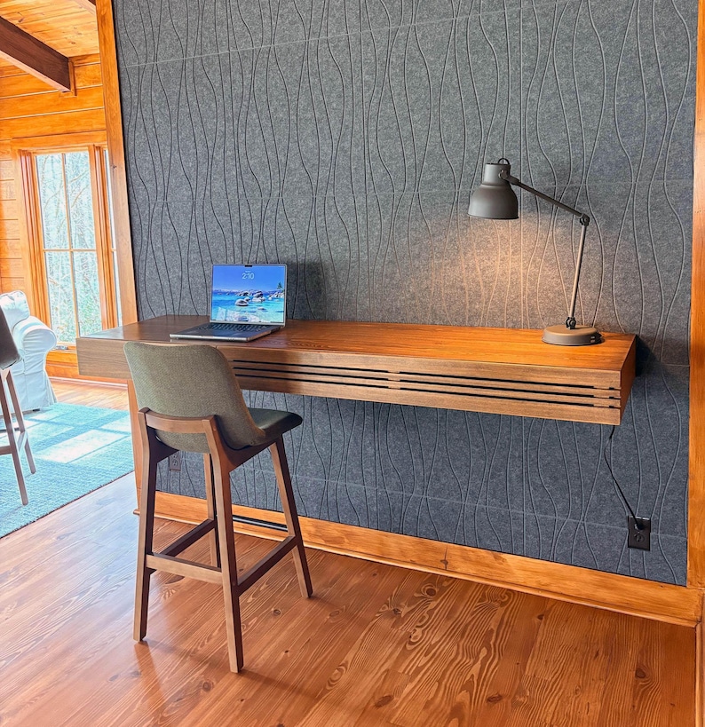 Peut inclure: Un bureau moderne en bois, fix&eacute; au mur, avec un ordinateur portable et une lampe de bureau. Le bureau a un design &agrave; lattes et est associ&eacute; &agrave; un tabouret de bar rembourr&eacute; vert. Le fond pr&eacute;sente un mur gris textur&eacute;.