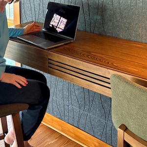 Peut inclure: Un bureau moderne en bois avec un tiroir int&eacute;gr&eacute; et un ordinateur portable. Le bureau est fix&eacute; &agrave; un mur textur&eacute; gris. Une chaise verte est positionn&eacute;e pr&egrave;s du bureau. Le bureau est en bois avec une finition naturelle.