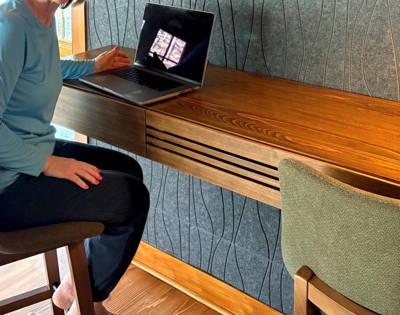 Peut inclure: Un bureau moderne en bois avec un tiroir int&eacute;gr&eacute; et un ordinateur portable. Le bureau est fix&eacute; &agrave; un mur textur&eacute; gris. Une chaise verte est positionn&eacute;e pr&egrave;s du bureau. Le bureau est en bois avec une finition naturelle.