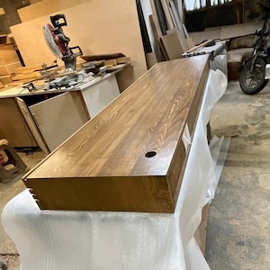 Peut inclure: Un bureau rectangulaire en bois avec une finition naturelle vein&eacute;e. Le bureau a une teinture brun fonc&eacute; et un trou circulaire &agrave; la surface. Le bureau est pos&eacute; sur une surface blanche.