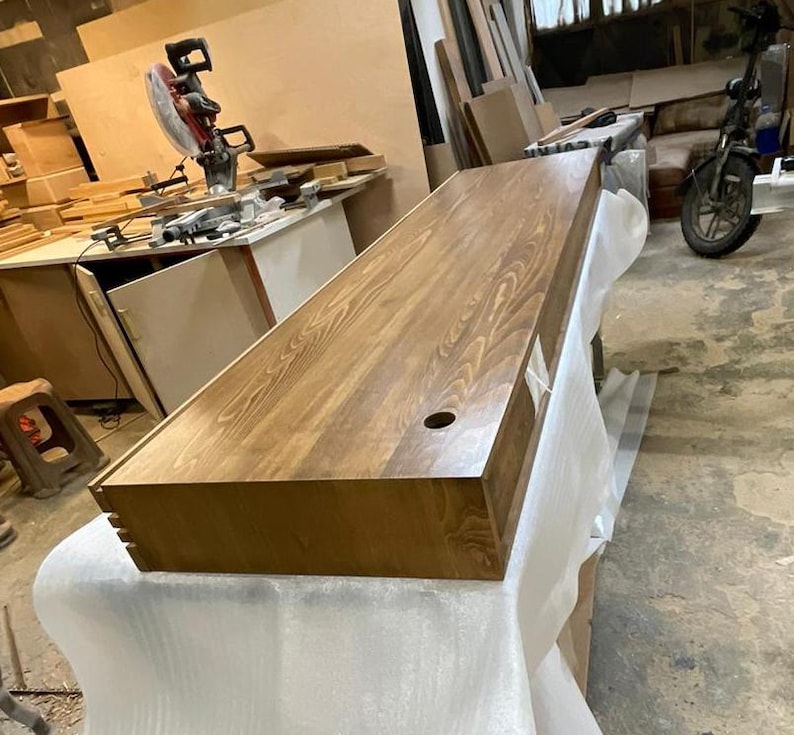 Peut inclure: Un bureau rectangulaire en bois avec une finition naturelle vein&eacute;e. Le bureau a une teinture brun fonc&eacute; et un trou circulaire &agrave; la surface. Le bureau est pos&eacute; sur une surface blanche.