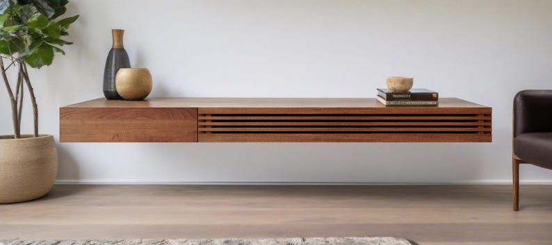 May include: A wooden floating shelf with a drawer and slatted design. The shelf is mounted on a white wall and has two decorative vases and a bowl on top.