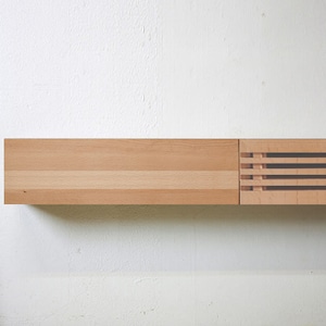 May include: A wooden shelf with a decorative slatted panel on the right side. The shelf is made of light wood and is mounted on a white wall.