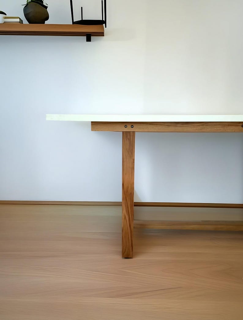 K&ouml;nnte beinhalten: Ein moderner Holztisch mit wei&szlig;er Tischplatte. Der Tisch hat vier stabile Holzbeine und eine hellbraune Oberfl&auml;che. Der Tisch steht vor einer wei&szlig;en Wand und einem hellbraunen Holzboden.