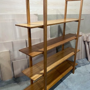 May include: A wooden bookshelf with four shelves and a rectangular frame. The shelves and frame are made of light brown wood. The bookshelf is angled slightly, showing the side and front.