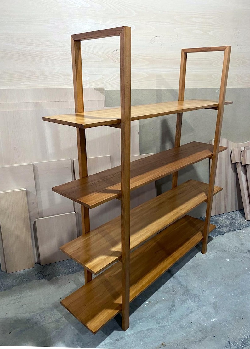 May include: A wooden bookshelf with four shelves and a rectangular frame. The shelves and frame are made of light brown wood. The bookshelf is angled slightly, showing the side and front.