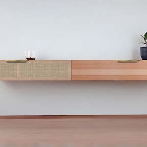 May include: A wall-mounted wooden shelf with two drawers. The left drawer is covered in a woven fabric and has a brass pull. The right drawer is made of wood and has a brass pull. A small potted plant sits on the top of the shelf.