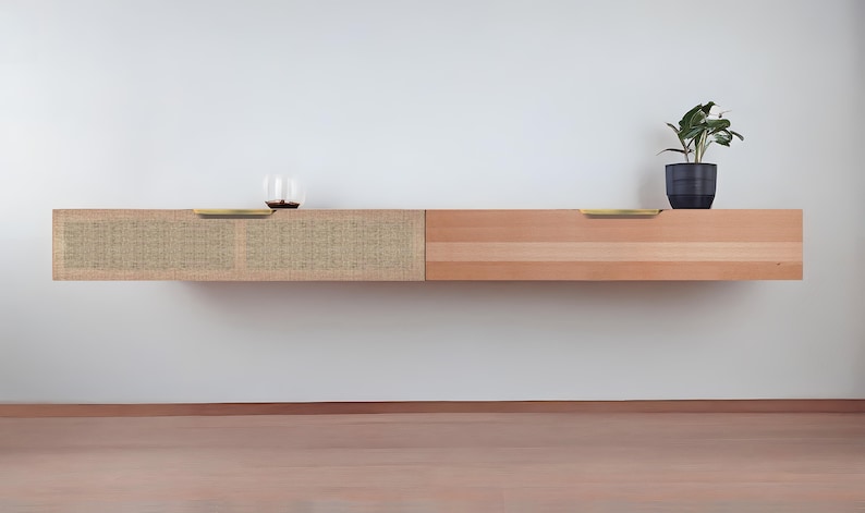 May include: A wall-mounted wooden shelf with two drawers. The left drawer is covered in a woven fabric and has a brass pull. The right drawer is made of wood and has a brass pull. A small potted plant sits on the top of the shelf.