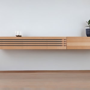 May include: A light wood wall mounted shelf unit with a slatted front and a solid wood side panel. A small potted plant sits on the top of the shelf.