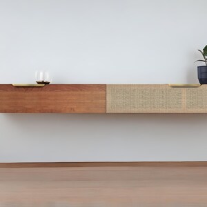May include: A floating wall shelf with two sections. The left section is made of dark wood and the right section is made of woven natural fiber. Both sections have brass pulls.