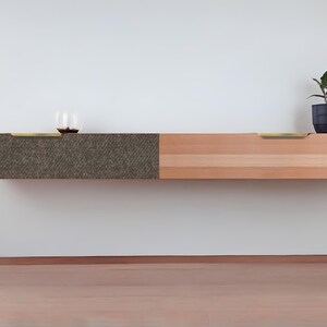 May include: A floating wall shelf with two drawers. The left drawer is covered in a dark brown textured material. The right drawer is made of light wood with a natural grain. Both drawers have brass pulls.