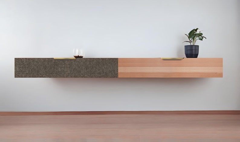 May include: A floating wall shelf with two drawers. The left drawer is covered in a dark brown textured material. The right drawer is made of light wood with a natural grain. Both drawers have brass pulls.