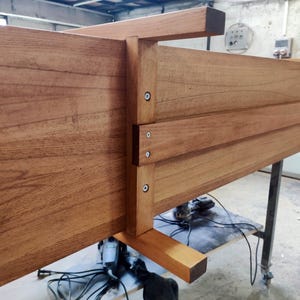 May include: A wooden furniture piece, possibly a bed frame or table, with a natural wood finish. The construction features visible joints and screws, showcasing a sturdy design. The wood grain is prominent, adding to the piece's rustic aesthetic.