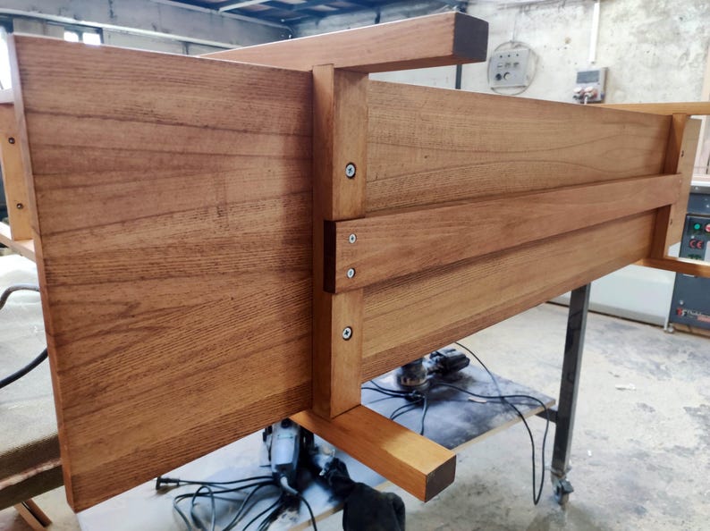 May include: A wooden furniture piece, possibly a bed frame or table, with a natural wood finish. The construction features visible joints and screws, showcasing a sturdy design. The wood grain is prominent, adding to the piece's rustic aesthetic.