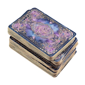Può includere: Un mazzo di carte dei tarocchi con un design celeste. I dorsi delle carte presentano una galassia ad acquerello nei toni del blu, viola e oro, incorniciata da un bordo blu scuro con dettagli dorati ornati. Il mazzo è impilato, mostrando i bordi dorati delle carte.