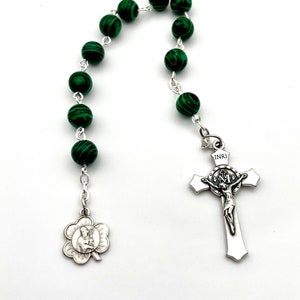 May include: A green malachite rosary with a silver crucifix and a silver shamrock charm. The crucifix features a depiction of Jesus Christ with the inscription "INRI".