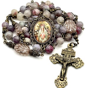 May include: A purple and white gemstone rosary with a bronze crucifix and a round pendant featuring a religious image. The pendant has a floral design and the text "JESUS NAZARENUS REX JUDAEORUM".