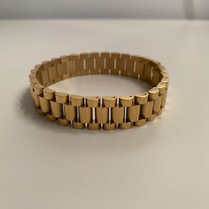 Op de afbeelding: Een gouden metalen armband met een schakellinkontwerp.