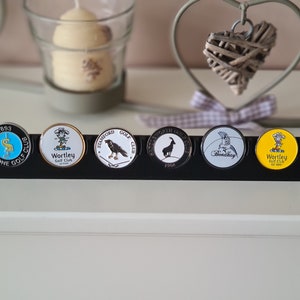 May include: A black display stand with six round golf ball markers. The markers feature different designs and logos, including a bird, a goat, and a golf club. The text on the markers includes "Silstone Golf Club", "Wortley Golf Club", "Stamford Golf Club", "Bondhay", and "Wortley Golf Club".