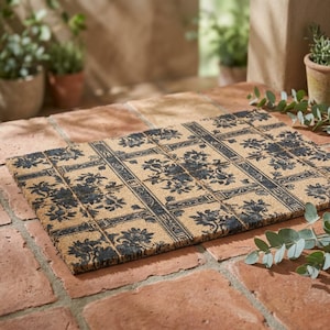 May include: Rectangular coir doormat with a floral and geometric pattern in navy blue on a natural tan background. The mat is placed on a brick surface, suitable for an entryway or outdoor space.
