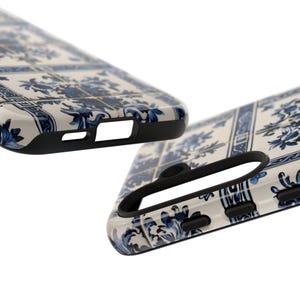 May include: Two phone cases with a white and blue floral tile pattern. The cases have a glossy finish and black edges. The design features a repeating pattern of blue flowers and leaves on a white background. The cases are angled to show the side and top details.