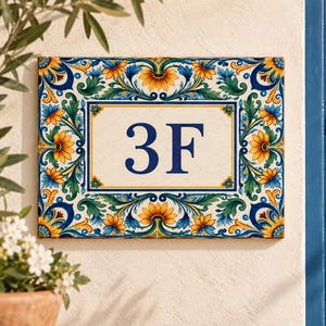 May include: A rectangular ceramic house number plaque featuring the text 3F in dark blue. The plaque is decorated with a vibrant border of yellow sunflowers, green leaves, and blue scrollwork patterns on a cream-coloured background.
